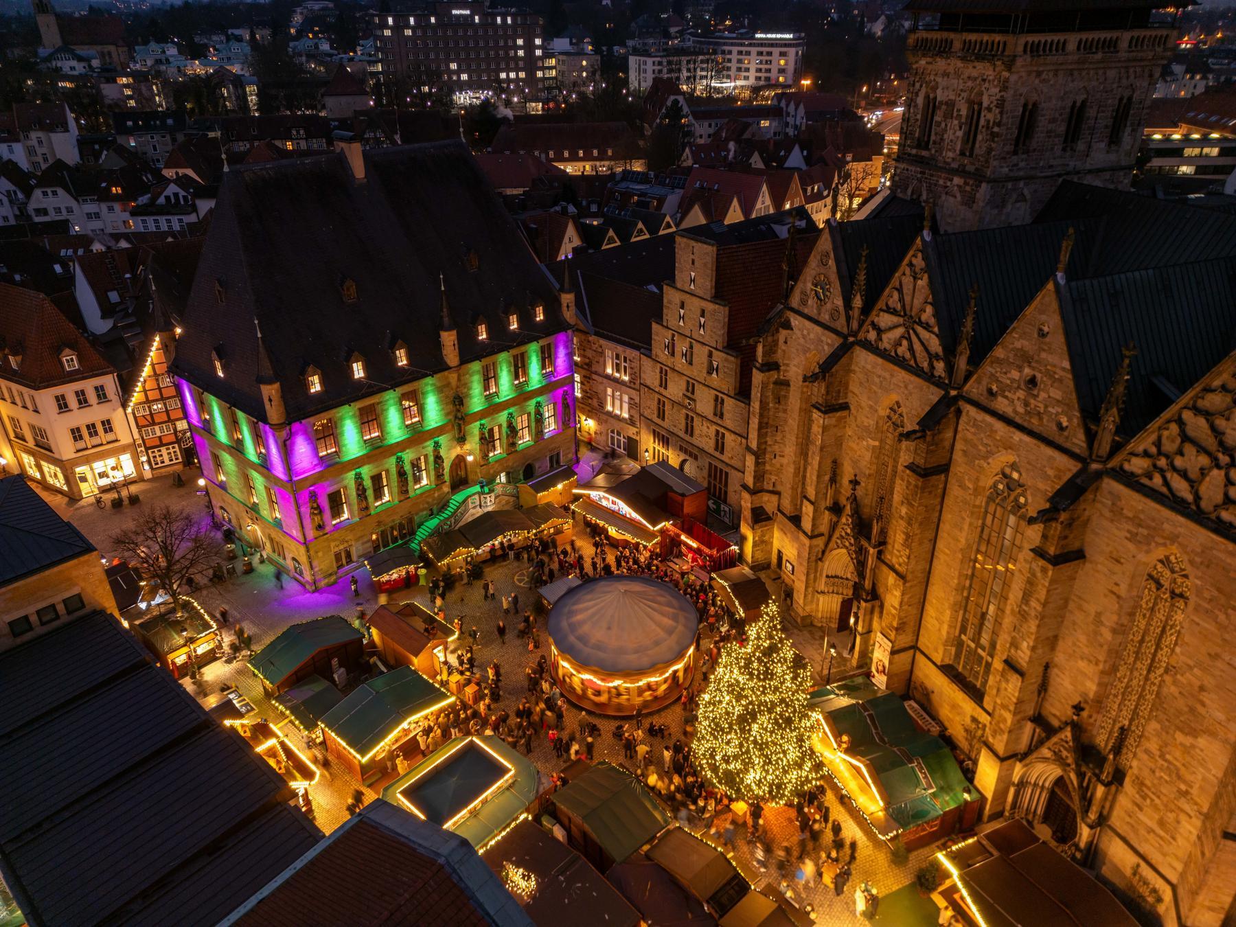 Historischer Weihnachtsmarkt: Gebäude mit bunter Beleuchtung, Weihnachtsbaum und Karussell auf dem Weihnachtsmarkt.