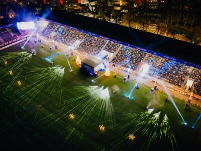 Volles Stadion beim Weihnachtssingen: Bühne, Lichter, festliche Stimmung. Besucherinnen und Besucher singen Weihnachtslieder.