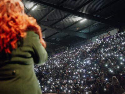 Weihnachtssingen: Menschenmenge hält leuchtende Handys in die Höhe, Blick auf Sängerin mit rotem Haar.