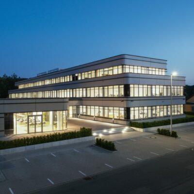 Bohnenkamp-Quadrat: Modernes, mehrstöckiges Bürogebäude mit großen Fensterfronten und beleuchtetem Eingangsbereich in der Abenddämmerung.