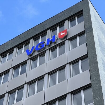 VGH Quadrat: Fassade des VGH Gebäudes mit blauem Logo und Wappen unter blauem Himmel. Bürogebäude Architektur.