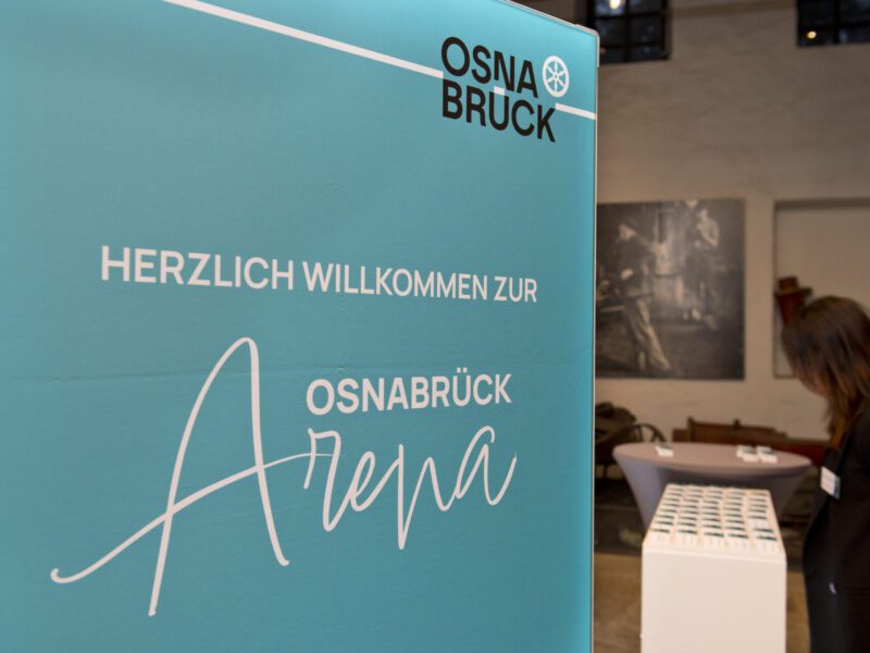 Ein blaues Willkommensschild mit der Aufschrift Arena und einem Logo in einem Raum mit einer Person am Empfangstisch