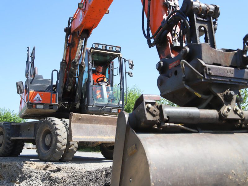 Dieckmann Baustelle Grothues Everswinkel Baggerfahrer im Führerhaus eines orangefarbenen Mobilbaggers mit Anbaugerät auf einer Baustelle