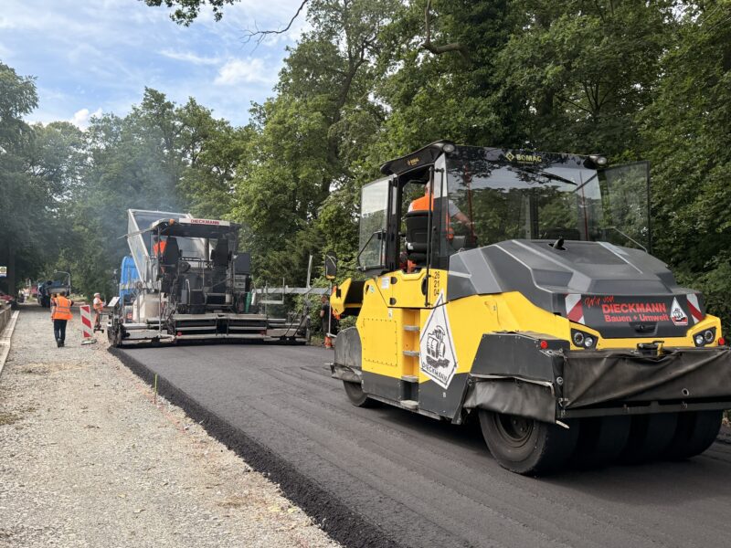 Arbeitsalltag 3 Asphaltarbeiten im Straßenbau: gelbe BOMAG Walze und Straßenfertiger beim Einbau von neuem Asphalt