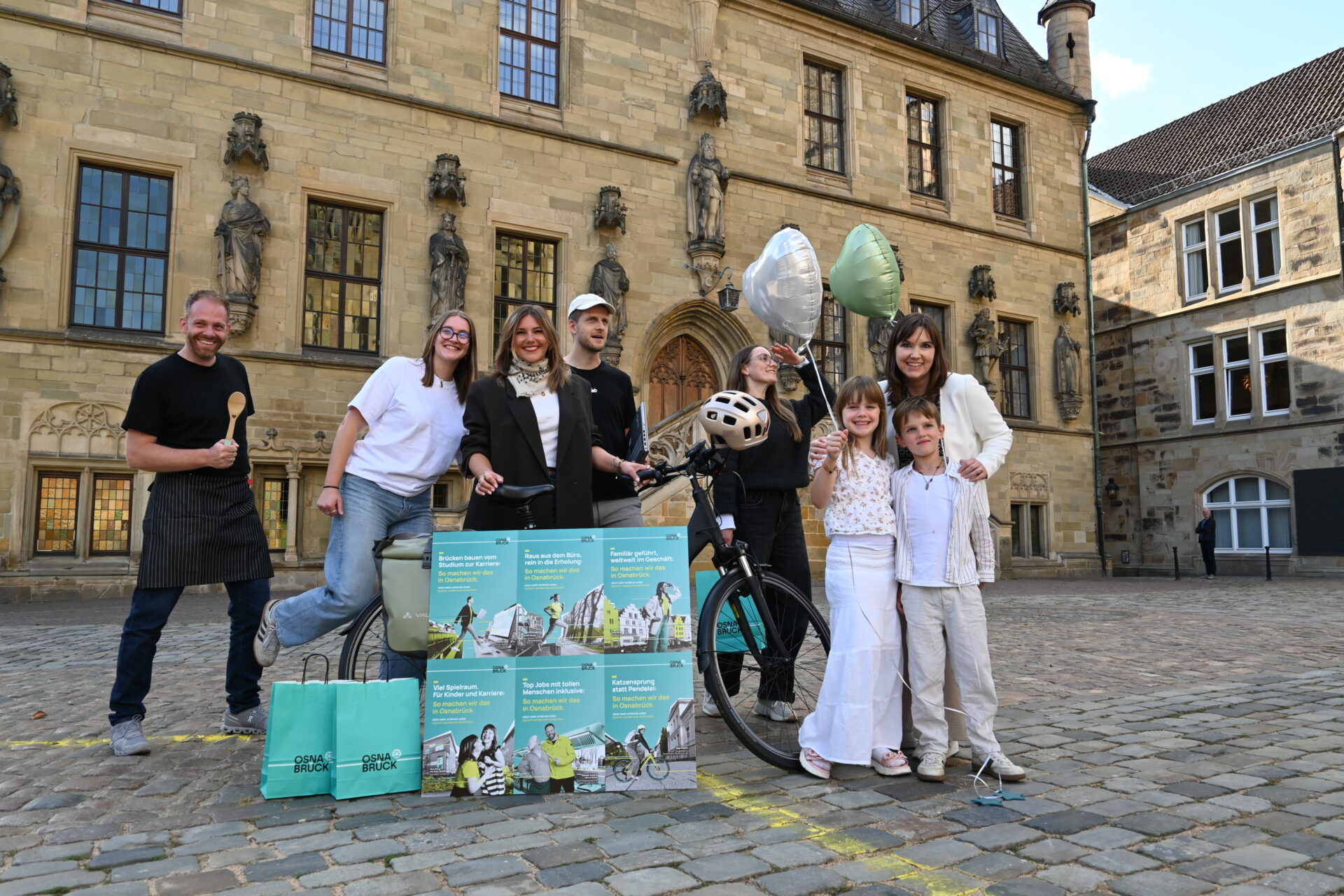 Gruppe von acht Menschen mit Fahrrad, Luftballons und Infomaterial vor historischem Gebäude