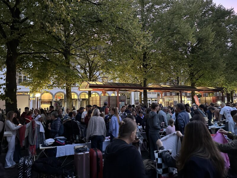 Nachtflohmarkt mit vielen Besuchern zwischen Bäumen und Verkaufsständen im Freien