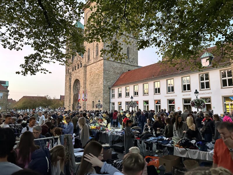 Menschenmenge auf einem nächtlichen Flohmarkt vor dem Dom, Stände mit Kleidung und Artikeln unter Bäumen
