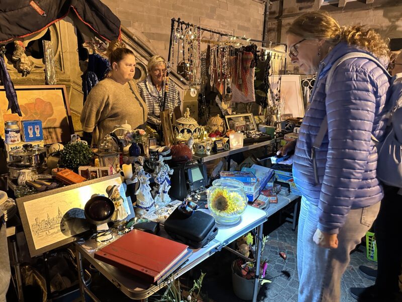 Besucherinnen stöbern bei einem Nachtflohmarkt an einem Stand mit Schmuck, Deko-Objekten und Trödel.